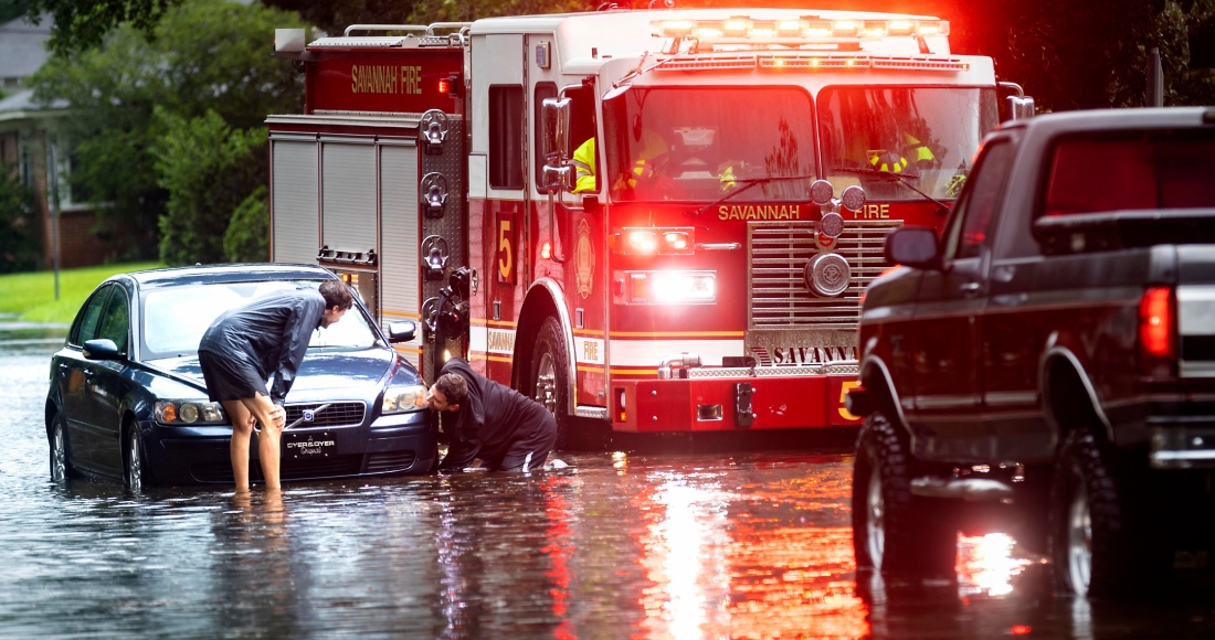 Dos personas atan un cabo a un auto varado en una calle anegada debido a las fuertes lluvias de la tormenta tropical Debby, el 5 de agosto de 2024, en Savannah, Georgia.