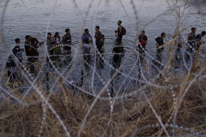 Migrantes esperan junto a una barrera de alambre