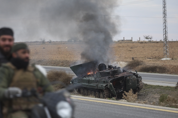 Rebeldes sirios pasan junto a un vehículo blindado incendiado al sur de Hama.