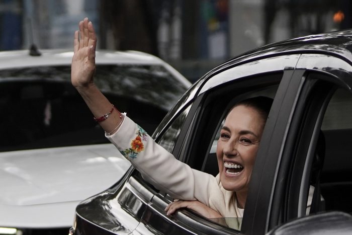 Claudia Sheinbaum saluda desde un vehículo en el que se dirige al Congreso.