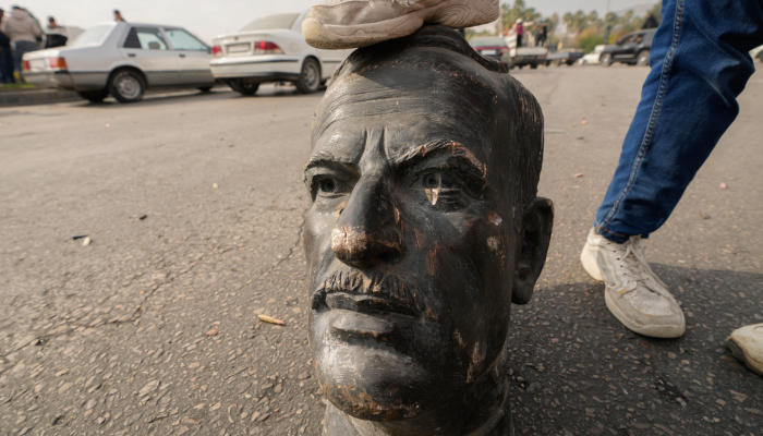 Un combatiente opositor pisa la cabeza de un busto roto del fallecido Presidente sirio Hafez Assad en Damasco, Siria, el domingo 8 de diciembre de 2024. 