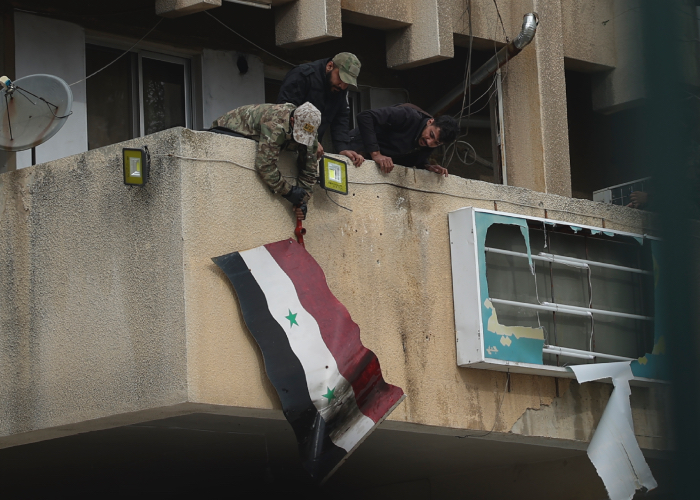 Sirios retiran una bandera del Gobierno, tras la caída de Bashar al Assad.