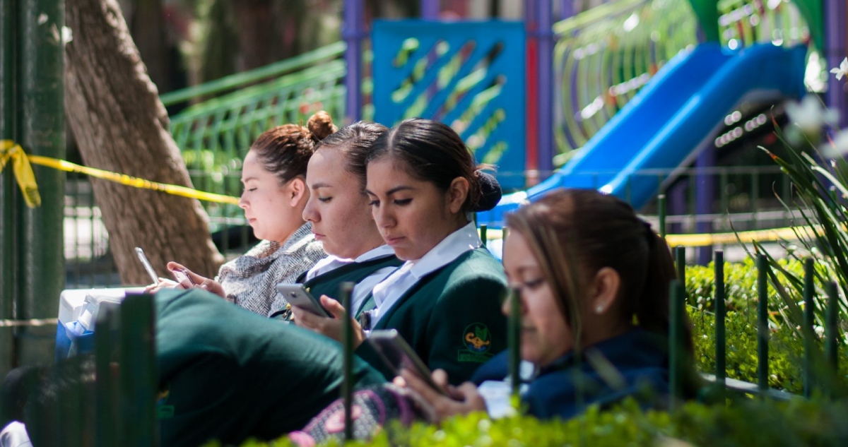 Cuatro mujeres utilizan su celular mientras descansan en una banca ubicada en calles de la Ciudad de México.