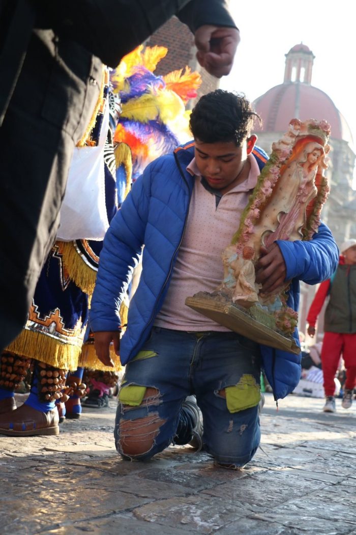 Un hombre sostiene una estatua de la Virgen de la Guadalupe mientras avanza de rodillas hacia la Basílica de Guadalupe.